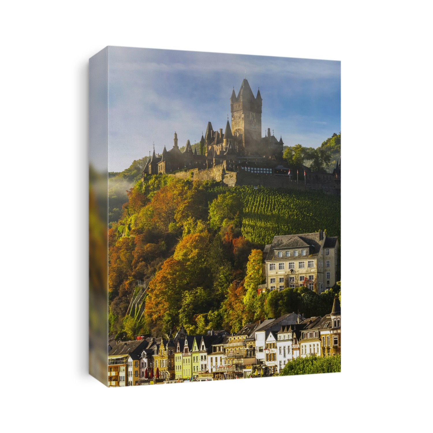 Large medieval castle on top of a colourful treed hillside with fog, blue sky, cloud and village below; Cochem, Germany
