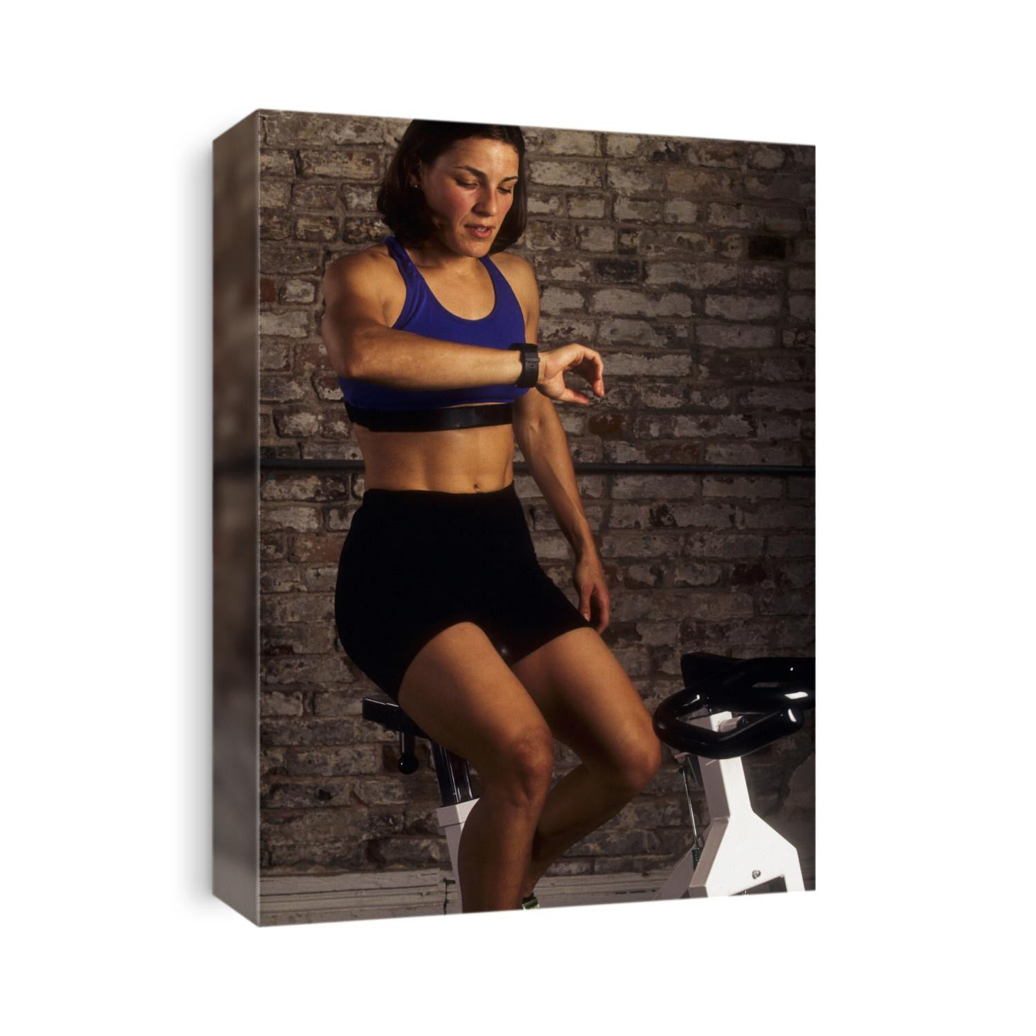 Young woman exercising on a stationary bike checking her heart rate.