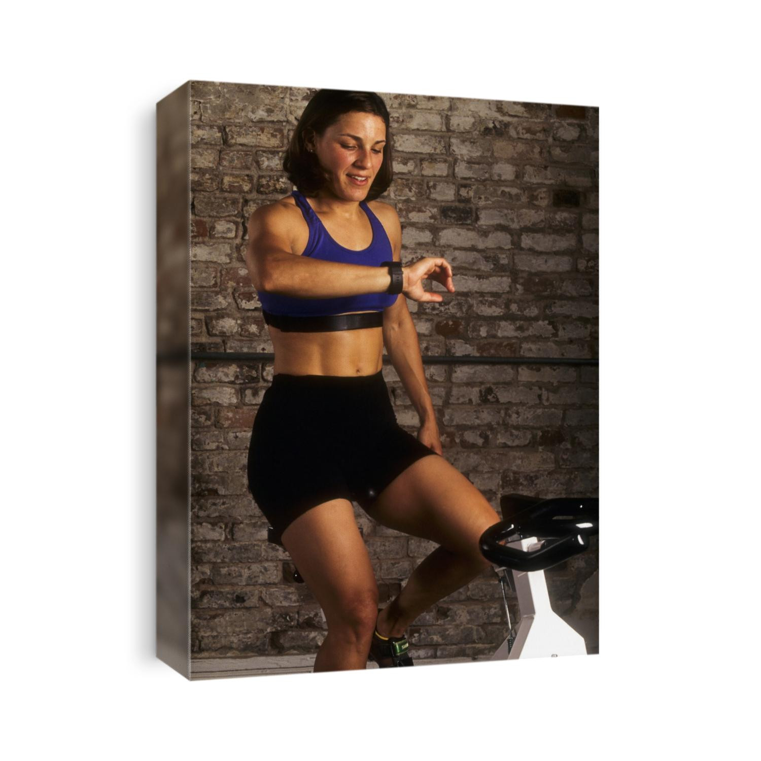 Young woman exercising on a stationary bike checking her heart rate.