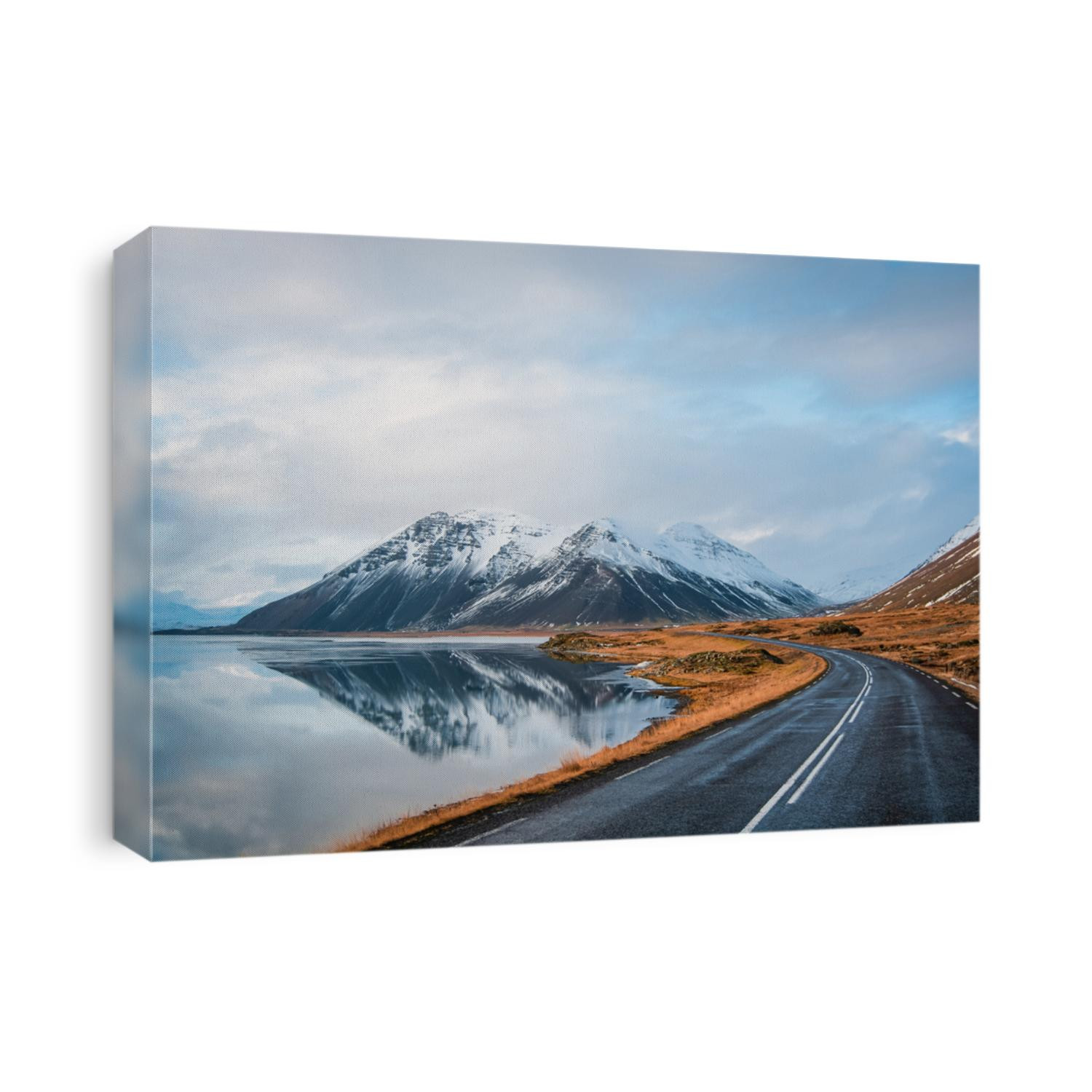 Panoramic winter photo of road leading along coast of lake to volcanic mountains. High rocky peaks covered with snow layer mirroring on water surface. Driver's point of view on Ring road, Iceland.