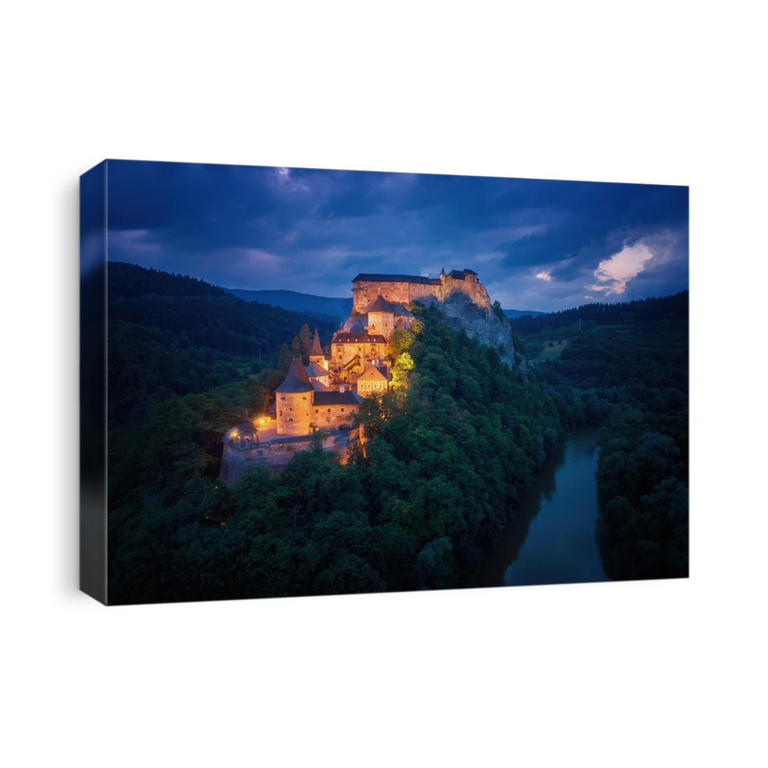 Aerial, dramatic view of Orava Castle, fantasy castle situated on a high rock above Orava river, illuminated by orange lamps against dark, cloudy background. Location used by movie makers. Slovakia.