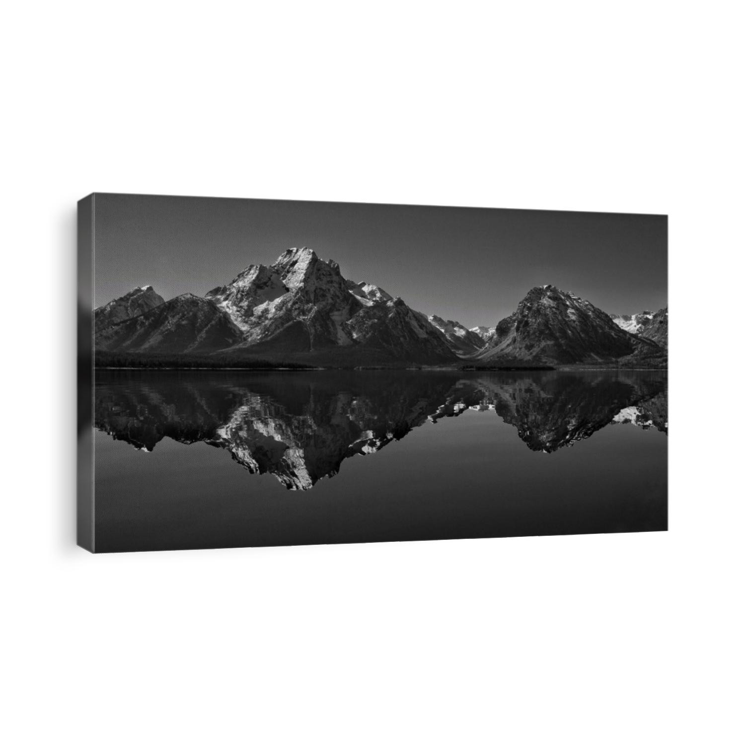 Beautiful black and white sweeping monochrome of the Grand Teton National Park, snow capped mountains and pine trees all reflected perfectly in Jackson Lake, taken from a kayak on a mirror surface!